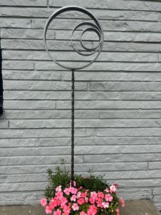 a planter with pink flowers in front of a white brick wall and metal spiral design