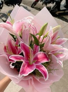 a bouquet of pink lilies is held by someone's hand on the sidewalk