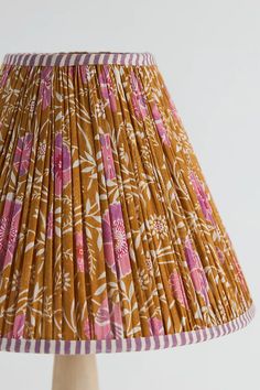 a lamp shade with pink and white flowers on brown fabric, sitting on a wooden base