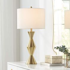 a gold lamp on a white table next to a mirror