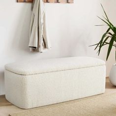 a white bench sitting in front of a wall mounted coat rack and potted plant