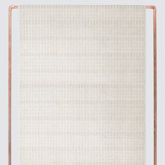 a white wall with a copper frame on it and a beige rug in the middle