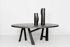 two black vases sitting on top of a wooden table in front of a white wall