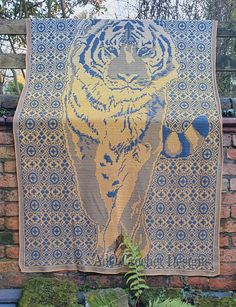 a blue and yellow tapestry with a tiger on it's face hanging from a brick wall