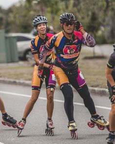 three men riding roller blades down the street together, one is wearing a helmet and holding his arm up to his ear