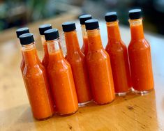 six bottles filled with hot sauce sitting on top of a wooden table next to each other