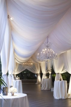 an indoor wedding venue with white draping and chandeliers