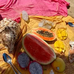 a watermelon and other fruits are on a towel next to a seashell