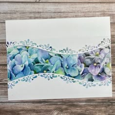 a card with watercolor flowers on it sitting on top of a wooden table next to a piece of paper