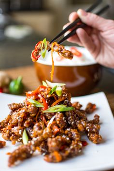 a person holding chopsticks over some food on a plate