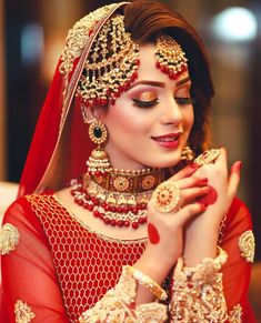 a woman in red and gold outfit with jewelry on her head, holding her hands to her chest