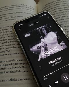 an open book with a cell phone displaying the west coast album on it's screen