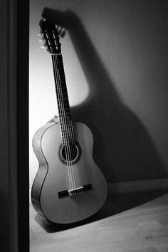 a black and white photo of a guitar leaning against a wall with its shadow on the wall