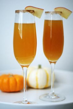 two glasses filled with liquid sitting on top of a white plate next to an orange pumpkin