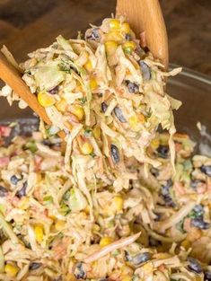 a bowl filled with coleslaw and corn on top of a wooden spoon