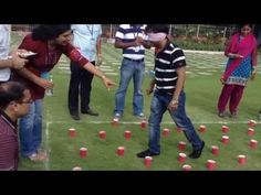 a group of people standing around cups on top of a grass covered field with one person pointing at them