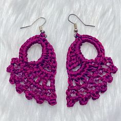 two pairs of crocheted earrings are shown on a white surface, one is pink and the other is purple