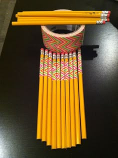 several yellow pencils lined up next to each other on a black table with a pink and green ribbon