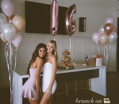 two beautiful young women standing next to each other in front of balloons and bunting