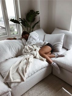 a woman laying on top of a white couch under a blanket next to a window