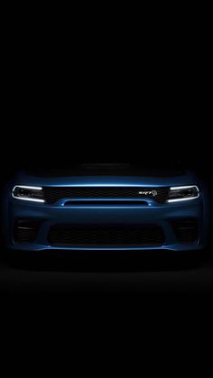 the front end of a blue dodge charger parked in a dark room with its lights on