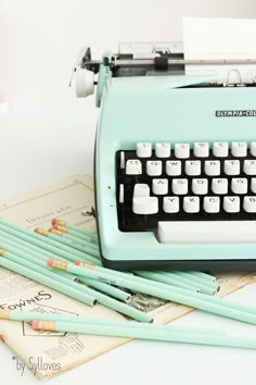 an old fashioned typewriter sitting on top of papers next to some pens and pencils