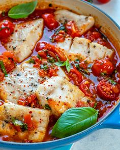 fish with tomatoes and basil in a blue pan