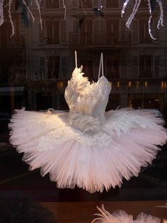 a white dress hanging in a window with feathers on the windowsill and chandelier behind it