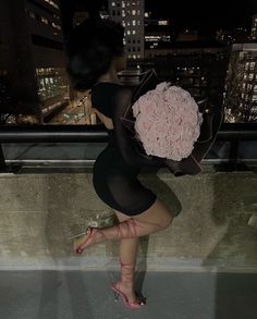 a woman holding a bouquet of flowers on top of a building in the city at night