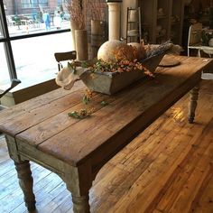 a wooden table topped with a bowl filled with flowers next to a large glass window