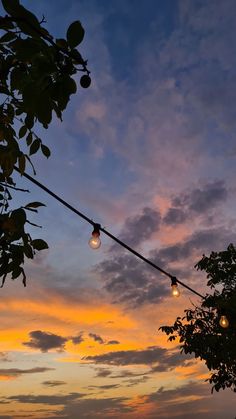 the sun is setting behind some trees with lights hanging from it's branches in front of an orange and blue sky