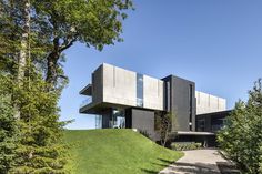 a modern house on top of a hill with trees and grass in the foreground