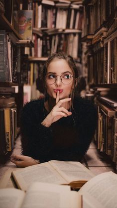 a woman sitting in front of a book shelf with her hand under her chin and looking at the camera