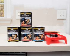 three cans of paint sitting on top of a counter next to a red tool and plastic container