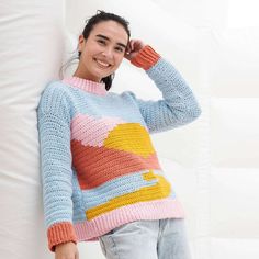 a woman leaning against a wall with her hand on her head wearing a colorful knitted sweater