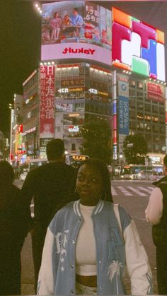 a woman standing in front of a tall building at night with people walking around it