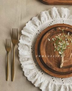 a wooden plate topped with flowers on top of a white doily next to gold utensils