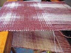 a weaving machine with red and white yarn on it's sides, next to a piece of wood