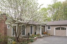 a house with two garages in front of it and trees around the driveway area