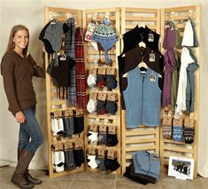 a woman standing in front of a wooden rack with sweaters and hats on it