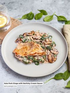 a white plate topped with chicken covered in mushrooms and spinach next to a glass of lemonade