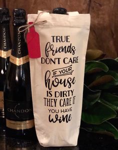 two bottles of wine sitting on top of a table next to a bag that says true friends don't care if your house is dirty they care if you have wine