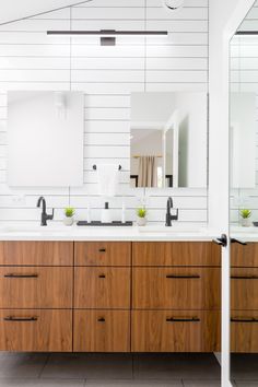 a bathroom with two sinks, mirrors and wooden cabinetry in the middle of it