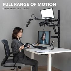 a woman sitting in front of a desk with a monitor and microphone on top of it