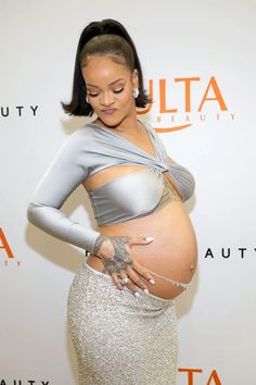 the pregnant woman is posing in her silver skirt and grey top with tattoos on her stomach