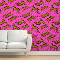 a white couch sitting in front of a pink wall with orange and black cats on it