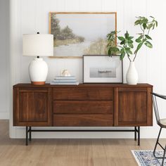 a wooden dresser with two vases on top of it next to a painting and lamp