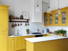 a kitchen with yellow cabinets and white counter tops, hanging lights above the stove top