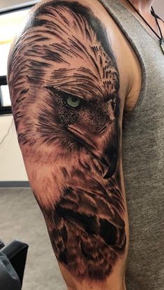 an owl tattoo on the arm and shoulder is shown in black and grey colors with green eyes