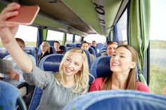 two women and one man are sitting on a bus with their arms in the air